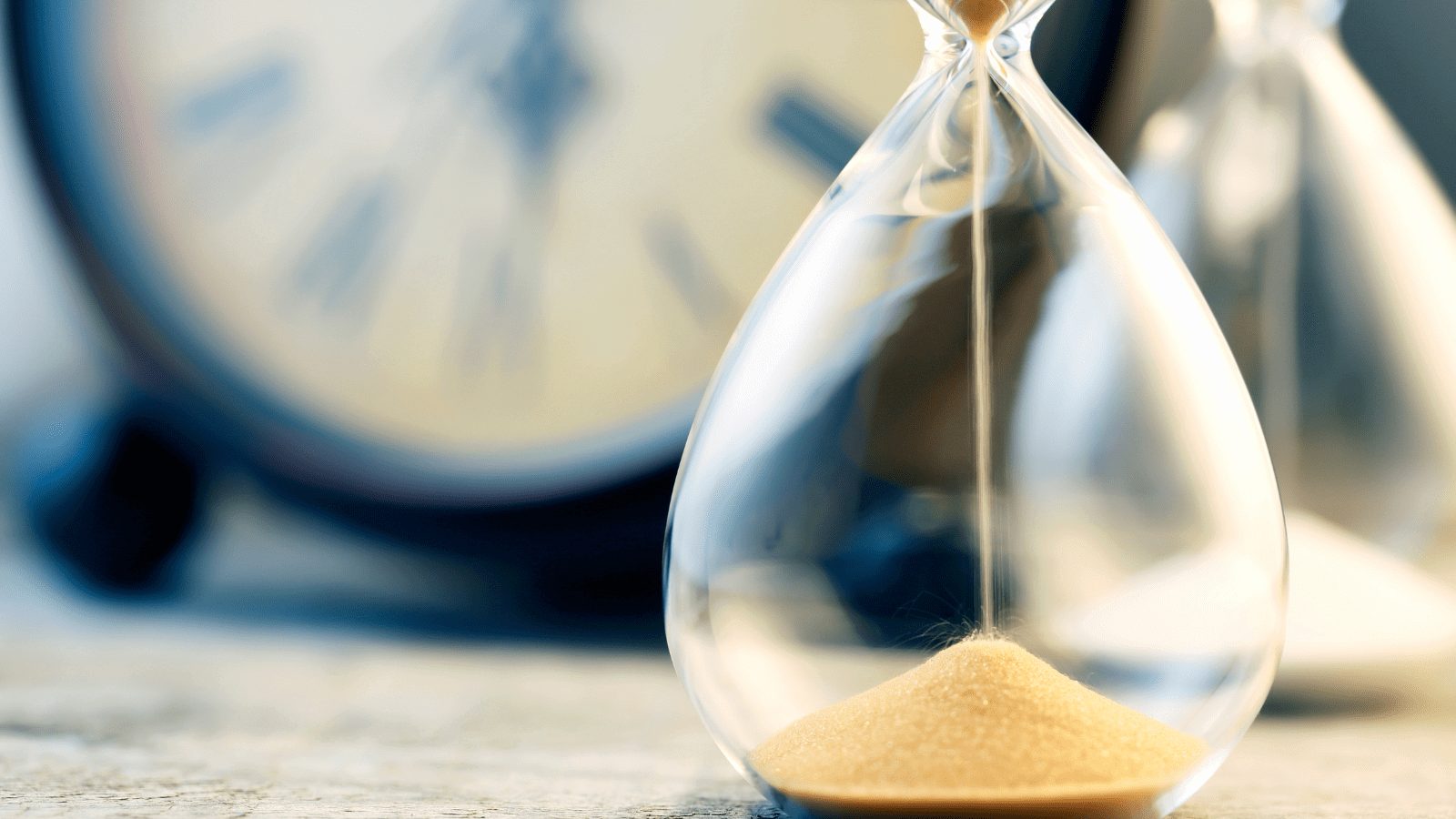 Hourglass with sand running out in front of a clock
