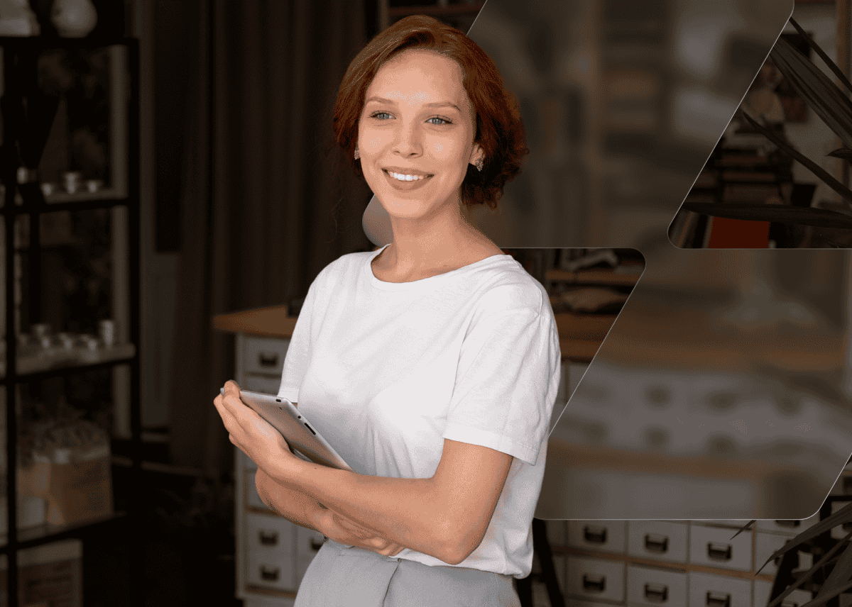 Smiling woman with short auburn hair holding a tablet with her arms crossed in a workshop