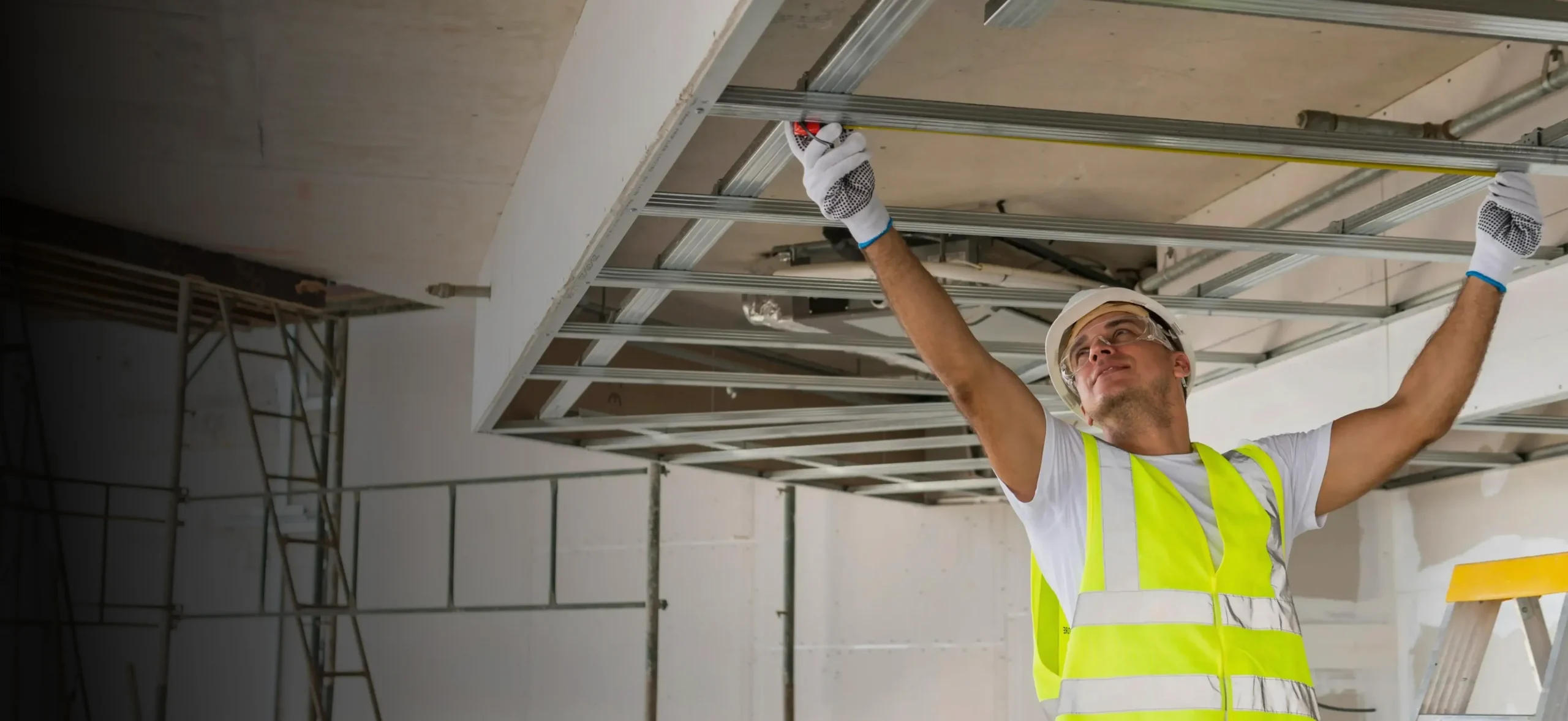 Contractor in a hard hat and safety vest installing a ceiling frame