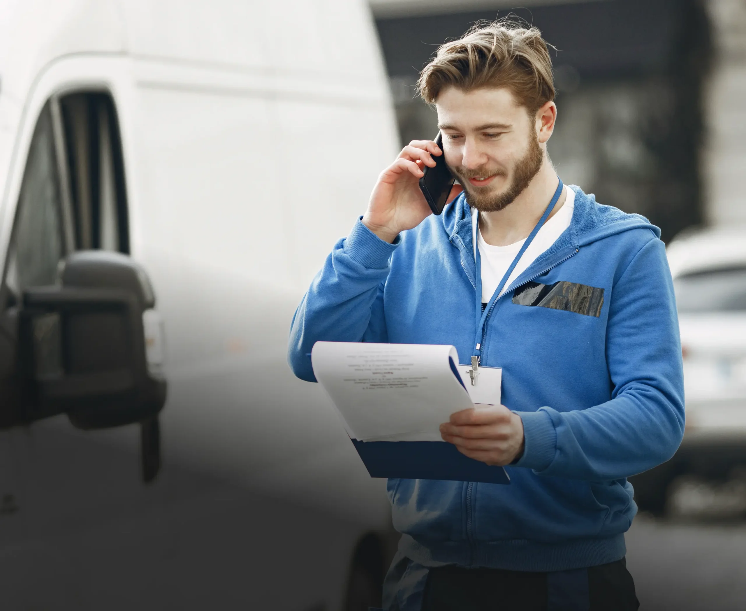 Fleet manager on the phone holding a clipboard beside a van