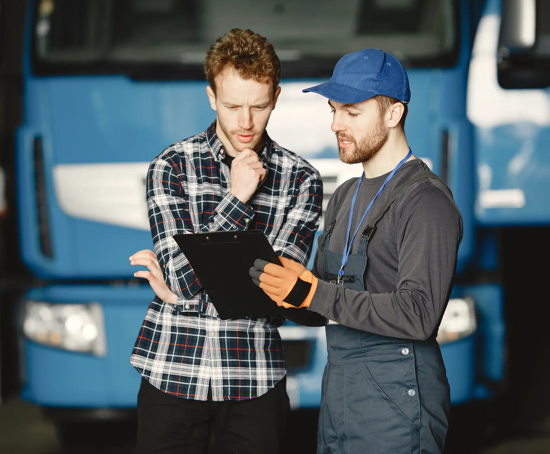 Two men reviewing a clipboard in front of a blue semi-truck inside a garage