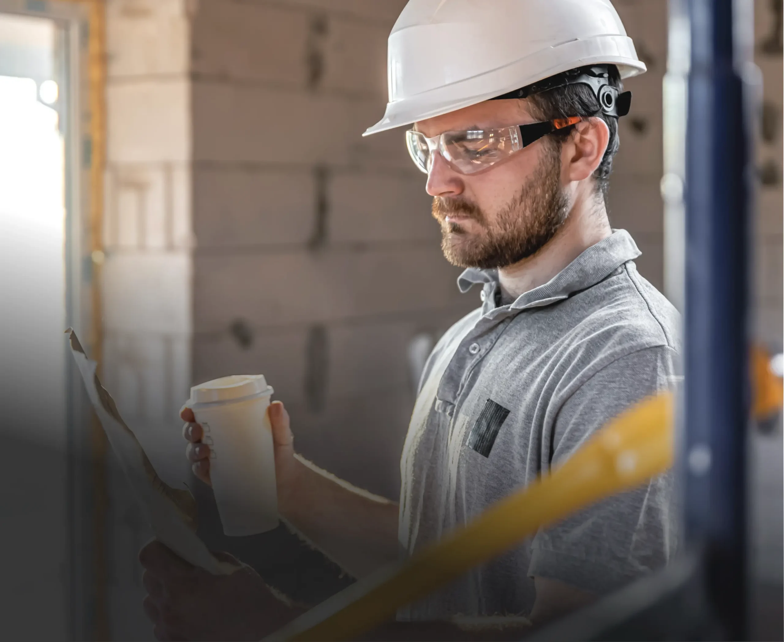 Contractor in a hard hat and safety glasses reviewing plans on site