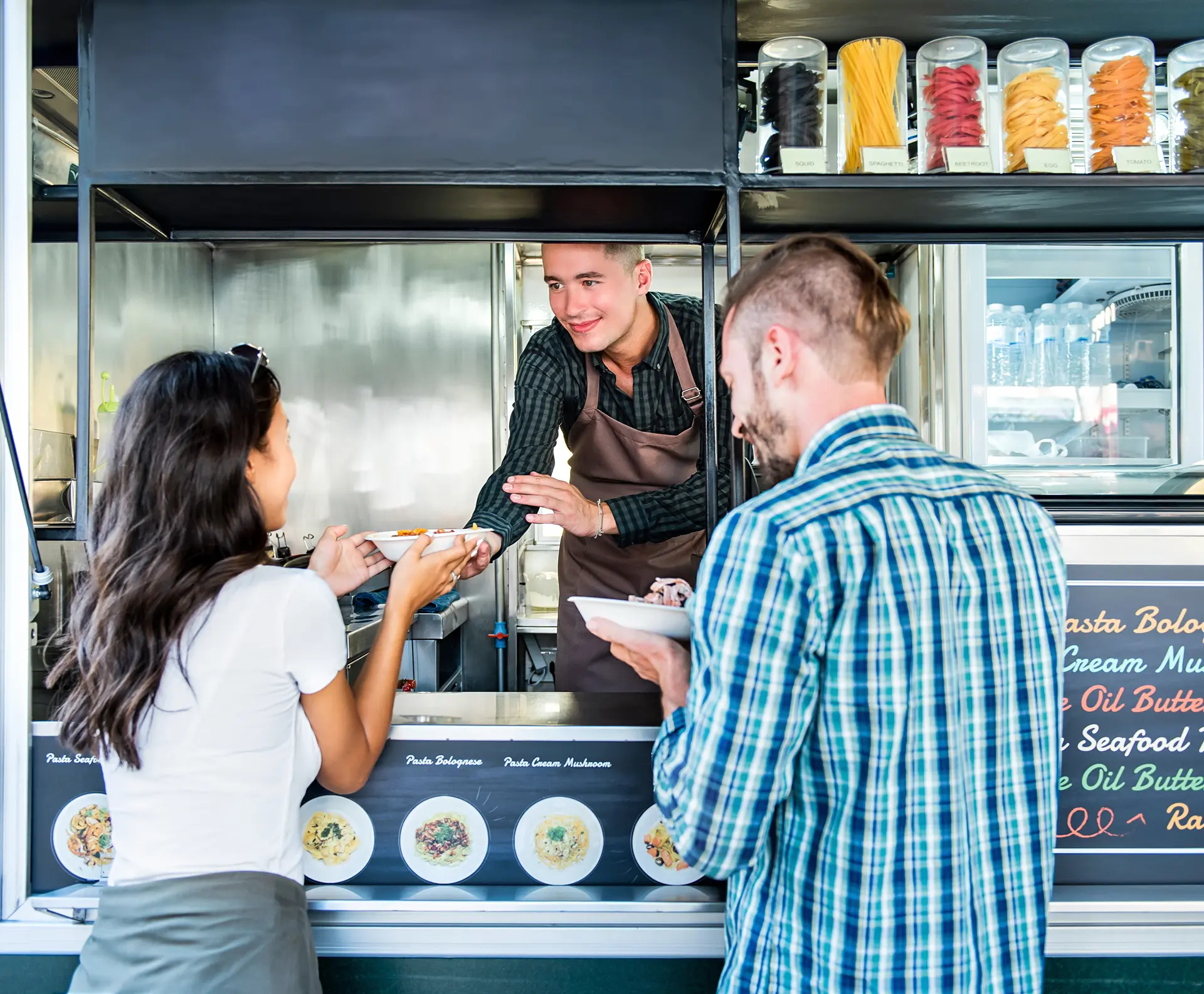 Food truck vendor handing a bowl of pasta to customers at the service window