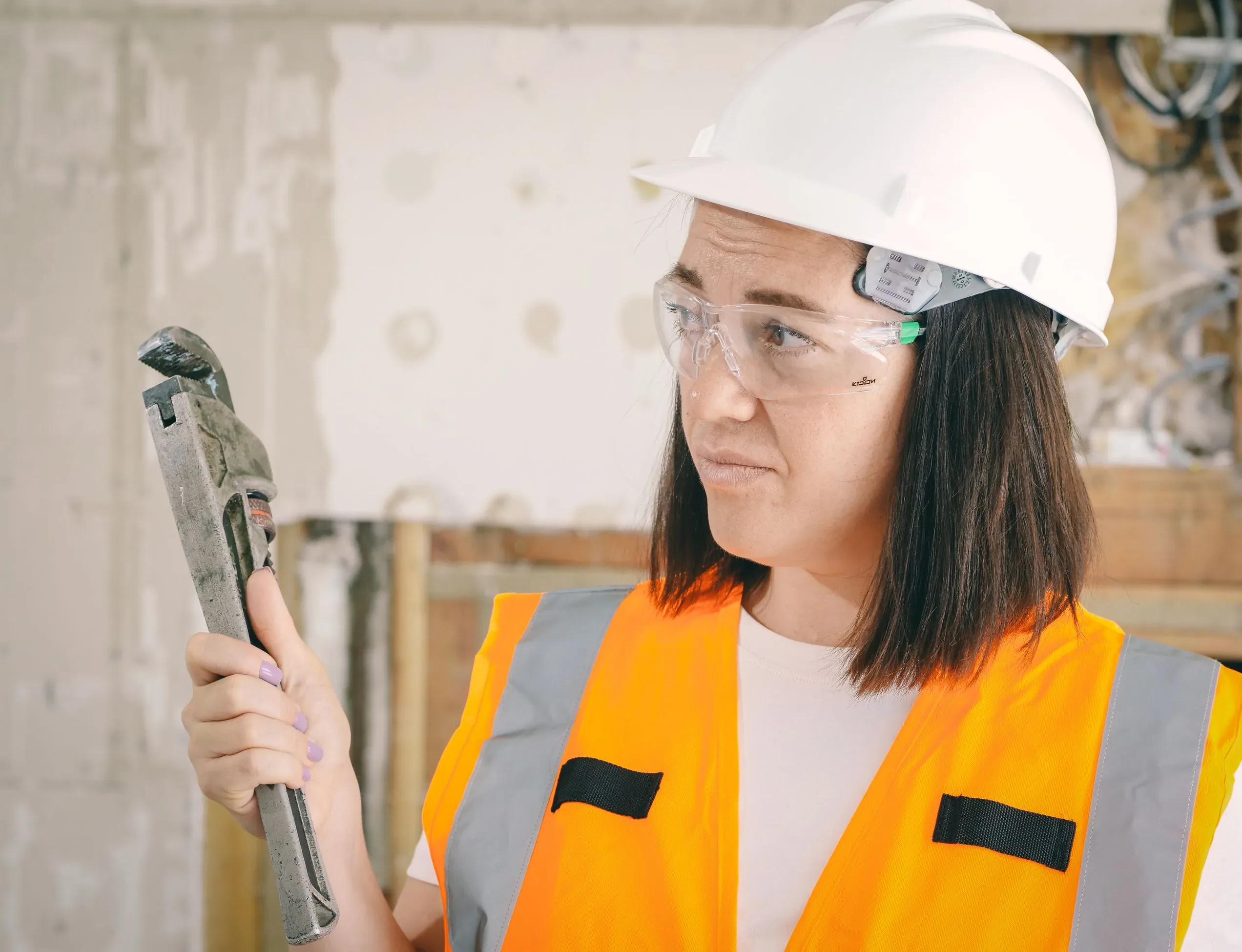 Plumber in a hard hat and safety vest holding a pipe wrench on a job site