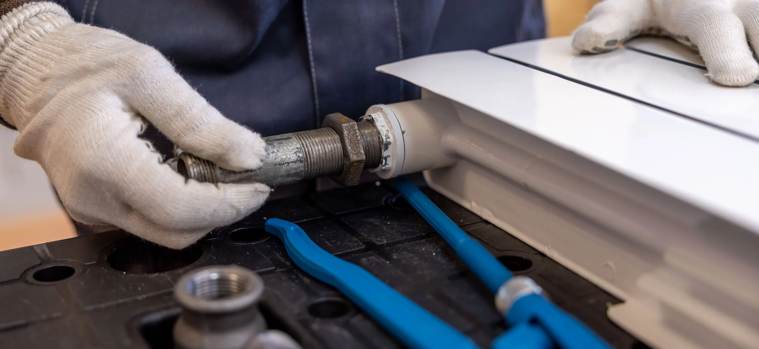 Plumber tightening a pipe fitting with gloved hands