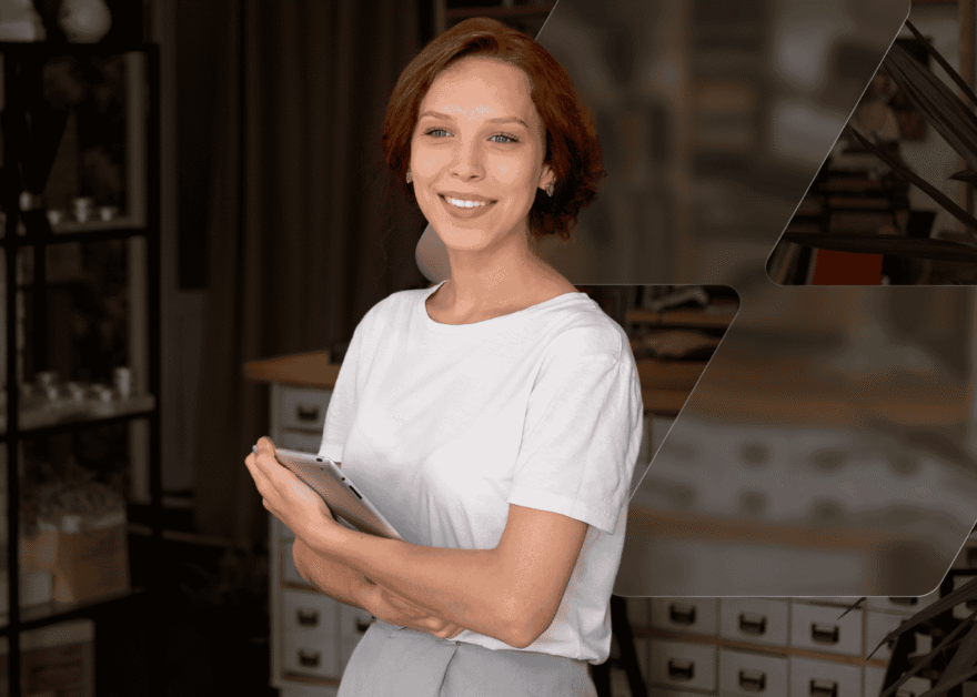 Smiling woman with short auburn hair holding a tablet with her arms crossed in a workshop