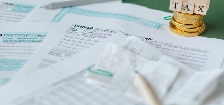 Stack of tax forms and coins with a 'TAX' stamp, symbolizing finance and accounting.