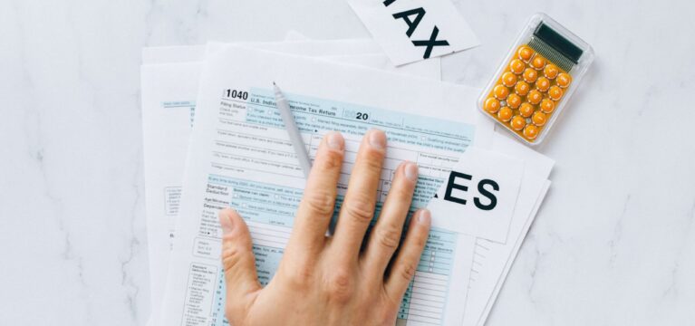Close-up of a hand on tax form 1040 with a calculator on a desk.
