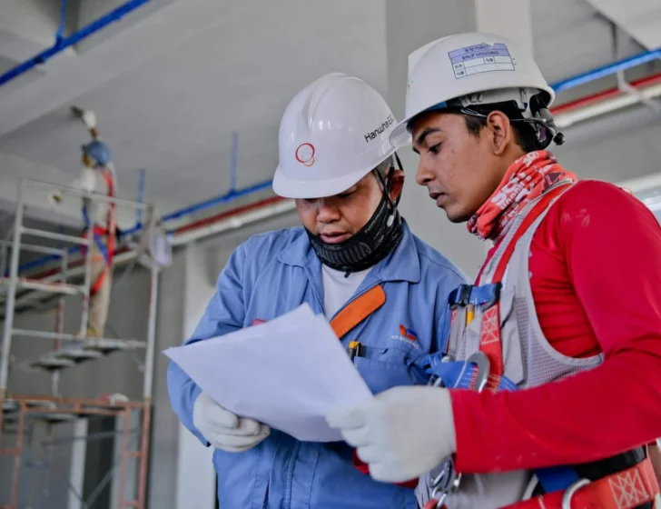 Two construction workers in hard hats reviewing plans on a job site