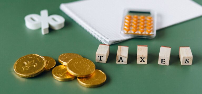 Gold coins, a calculator and wooden blocks spelling TAXES on a green desk