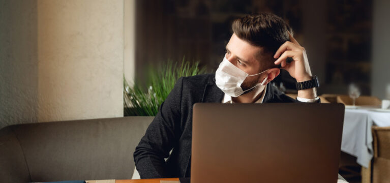 Bearded man in a face mask in a cafe with a laptop