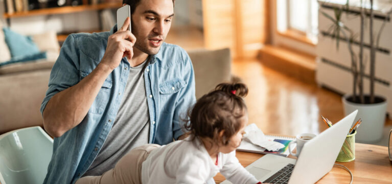 Young father babysitting while communicating on cell phone and working at home
