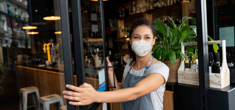 Happy business owner opening the door at a cafe wearing a facemask