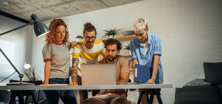 group of 4 people huddled around a desk looking at a laptop