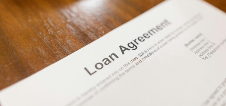 A close-up of a loan agreement document placed on a wooden surface, highlighting the title "Loan Agreement" in bold.