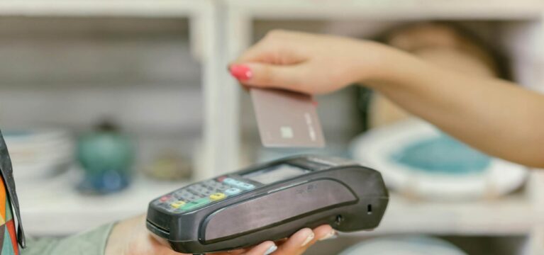 A customer holding a credit card near a point-of-sale (POS) terminal for a contactless payment in a retail setting.