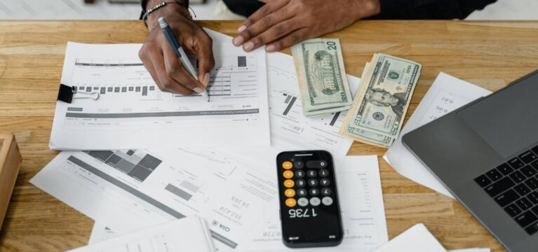 A person reviewing financial documents at a desk, with a calculator, cash, and a laptop nearby, illustrating business financial planning and cash flow management.