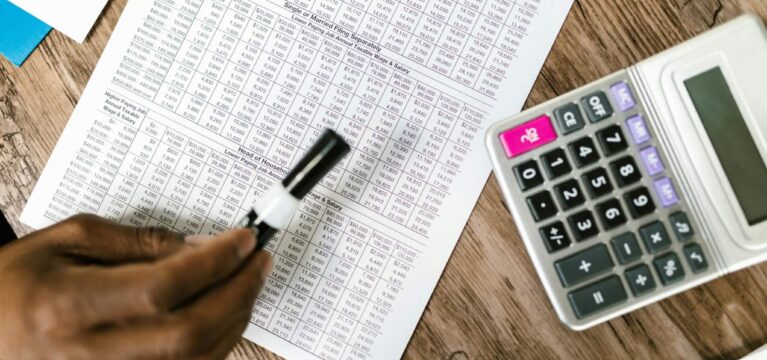 Close-up of a financial document with a pen and calculator on a wooden desk, symbolizing debt and income calculations.
