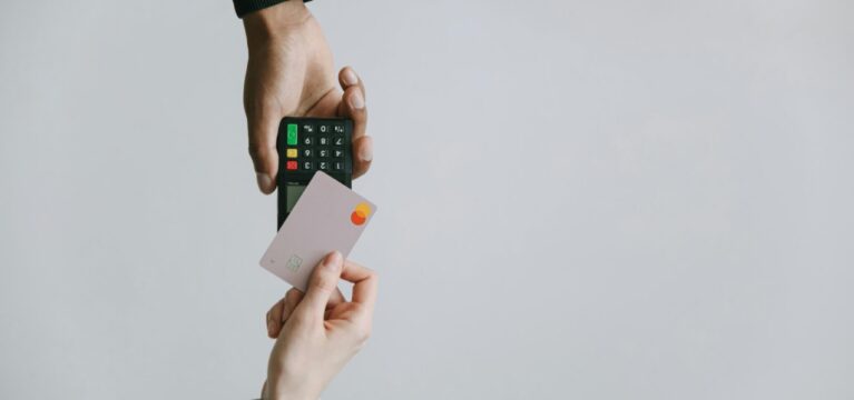 Close-up of a person holding a credit card while another person holds a card reader for payment.