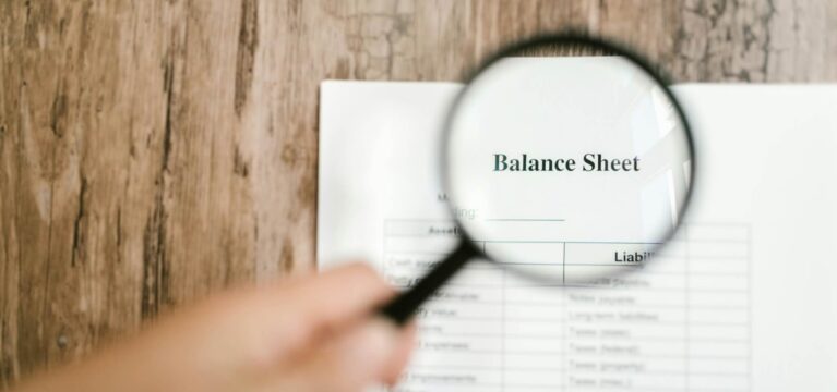 Magnifying glass over a sheet of paper displaying the words "balance sheet"