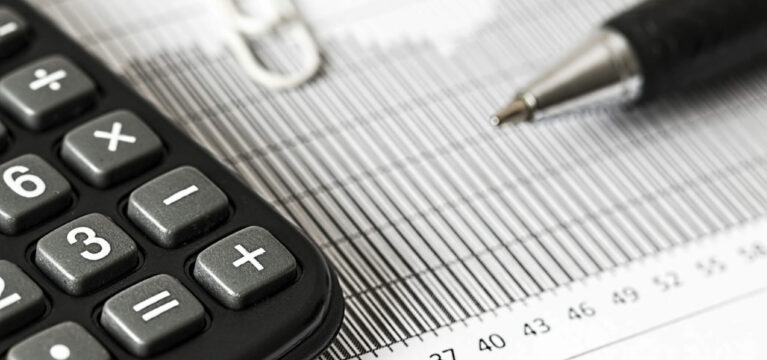 Close-up of a calculator, pen, and paper with numerical data and charts, representing financial analysis or accounting work.