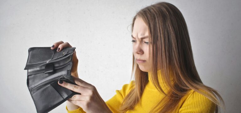 Woman in a yellow sweater looking concerned while examining an empty black wallet.
