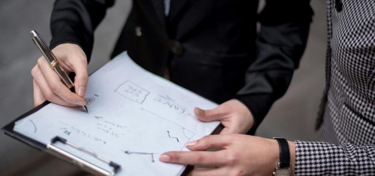 Two business professionals reviewing a financial plan on a clipboard, with handwritten notes and charts related to loan strategy.