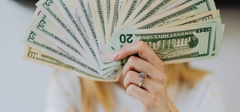 Woman holding a fan of U.S. dollar bills in front of her face, symbolizing business funding or financial success.